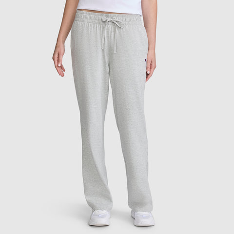 A person wearing Champion Lightweight Lounge Pants, C Logo in light gray, along with a white shirt and white sneakers, stands against a plain white background. Only the lower torso and legs are visible.