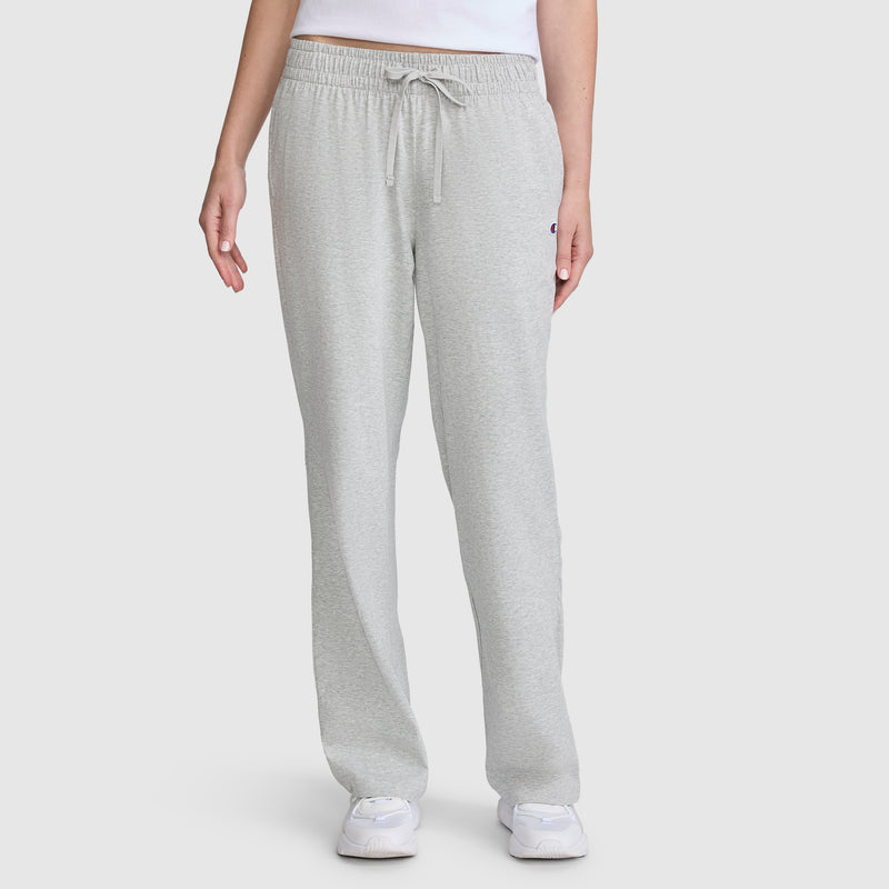A person wearing Champion Lightweight Lounge Pants, C Logo in light gray, along with a white shirt and white sneakers, stands against a plain white background. Only the lower torso and legs are visible.