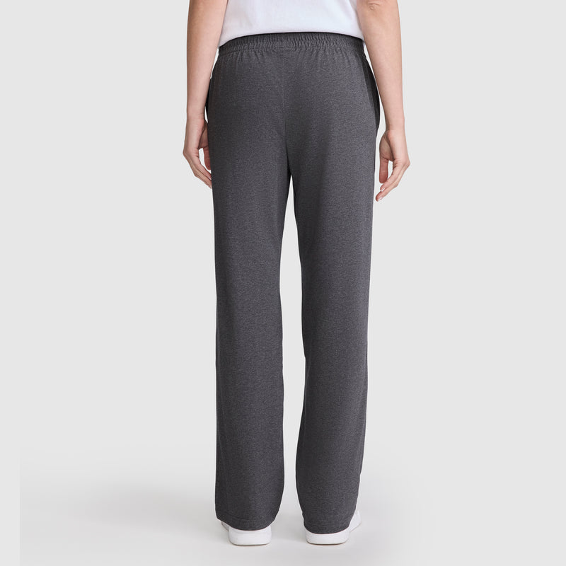A person stands with their back to the camera, wearing Champion’s Lightweight Lounge Pants, C Logo—dark gray, straight-leg, ultra-soft lounge pants featuring an elastic waistband for comfort—with a white top. The background is plain and light-colored.