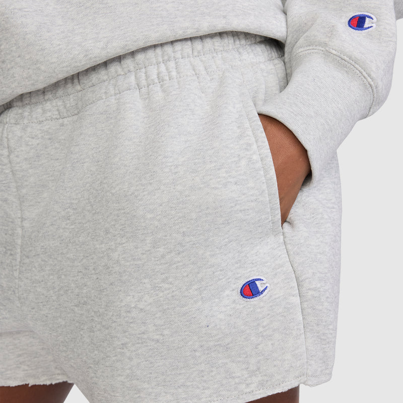 A person wears Champion's 3" Powerblend Shorts, C Logo in light gray along with a matching long sleeve sweatshirt. Both pieces display the signature blue and red Champion "C" logo for a classic touch. These comfortable Champion athletic shorts are ideal for everyday wear.
