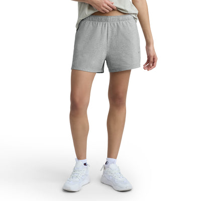 A person stands against a white background wearing a light grey T-shirt, Champion Practice Shorts, white socks, and white sneakers. The image is cropped at the shoulders so the face is not visible.