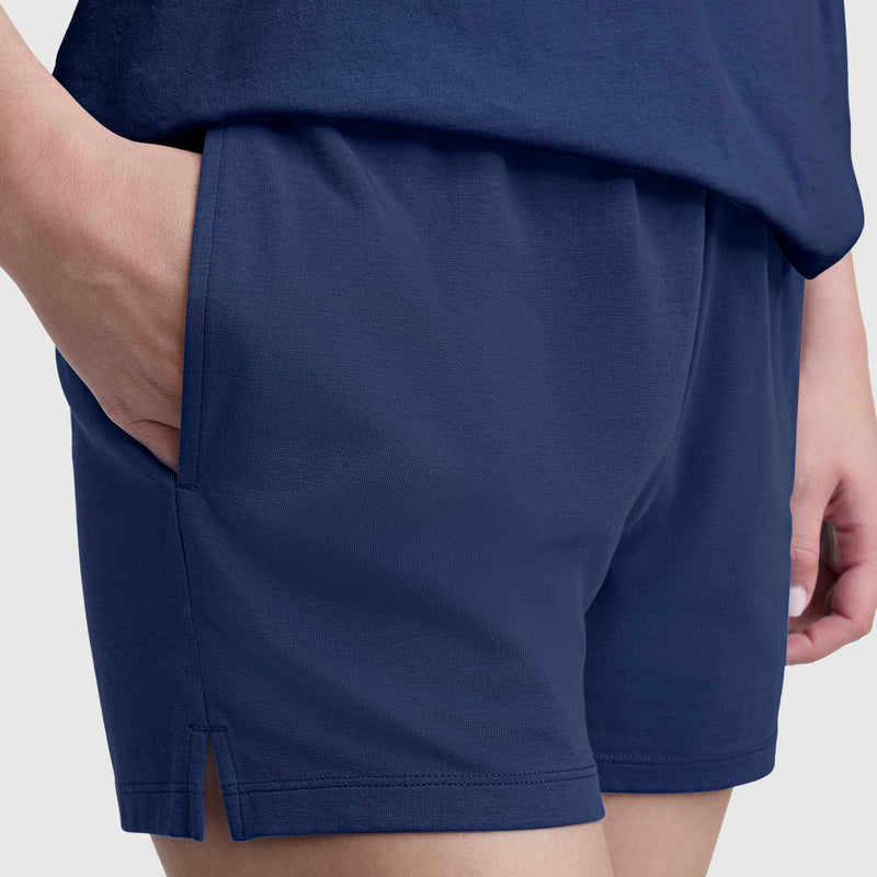 A person wearing Champion Practice Shorts for women in navy blue, with their right hand in the pocket, is shown from the waist to mid-thigh against a plain light background.