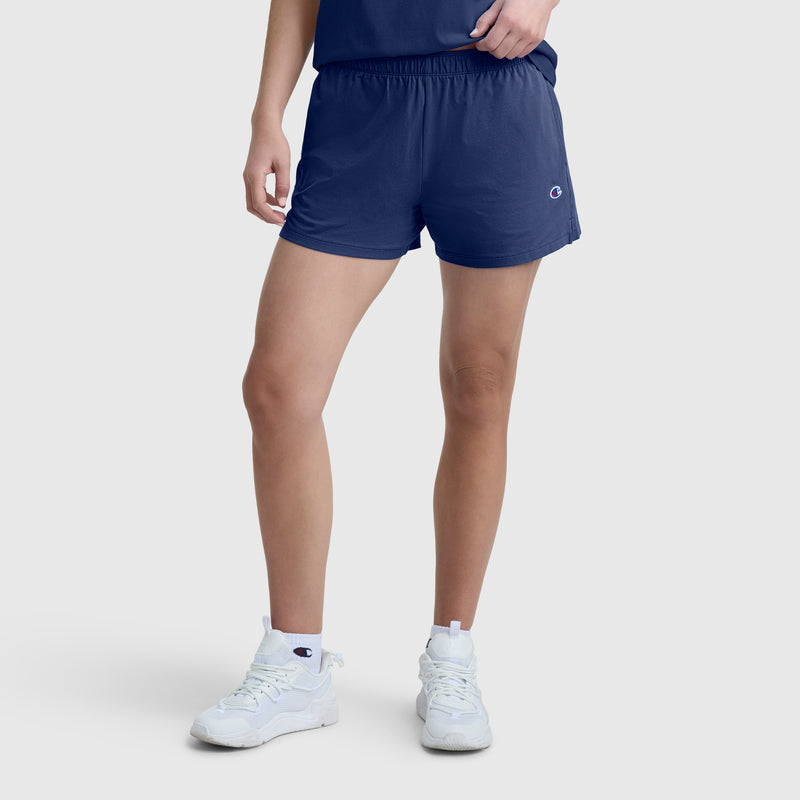 A person is wearing Champion Practice Shorts in navy, paired with a matching navy shirt and white high-top sneakers with a logo, standing against a plain light gray background. The person’s face is not visible.