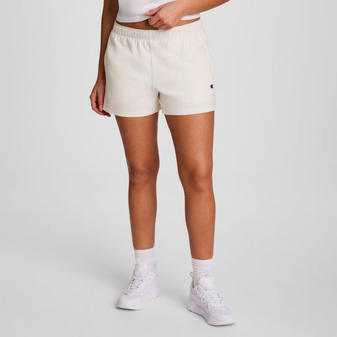 Wearing a white top, Champion Practice Short in cream, white socks, and sneakers, this person stands against a plain light gray background with hands at their sides and head out of frame—perfect comfy shorts for women.