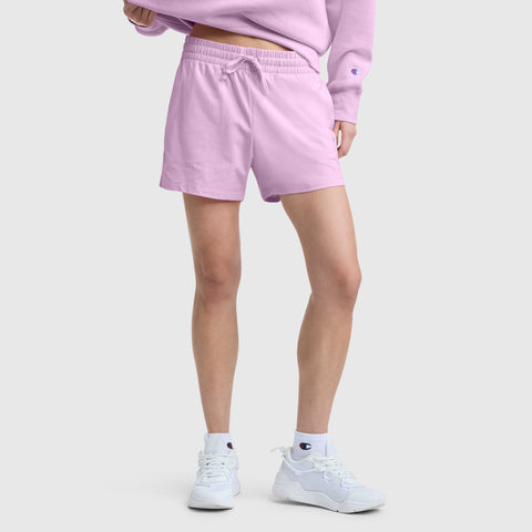 A person wearing the Champion 4″ Lightweight Lounge Shorts, C Logo in light pink paired with a matching sweatshirt and white sneakers. The image is cropped at the waist, showing only the lower half of the body against a plain light background.