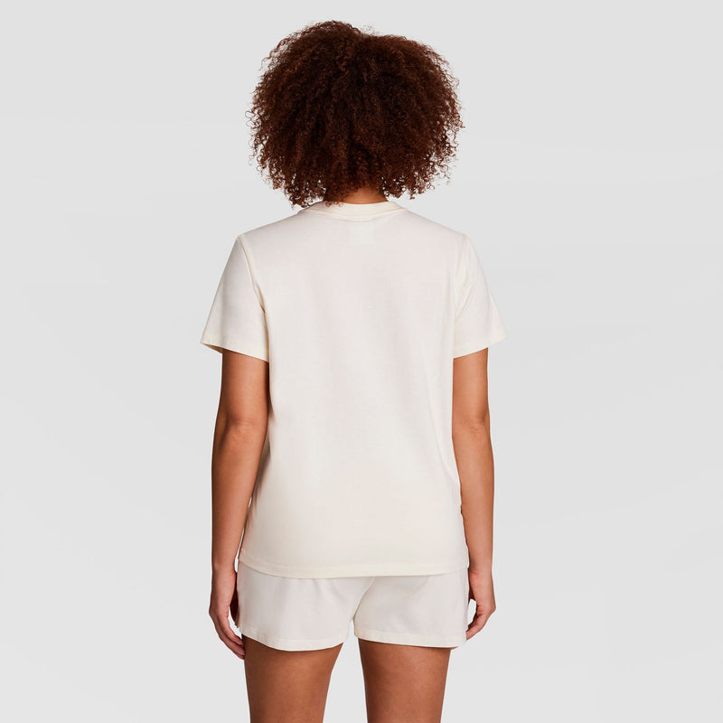 A person with curly hair, facing away from the camera, is wearing a Champion Classic T-Shirt with Tonal Left Chest Script and matching shorts against a plain light background.