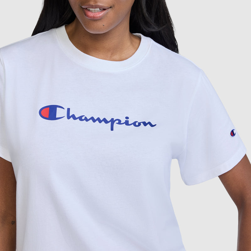 A woman models the Champion Classic T-Shirt, Script Logo in white, showcasing the brand's iconic blue and red script logo across the chest. The image is cropped from shoulders to mid-torso, emphasizing this stylish women's athletic shirt.