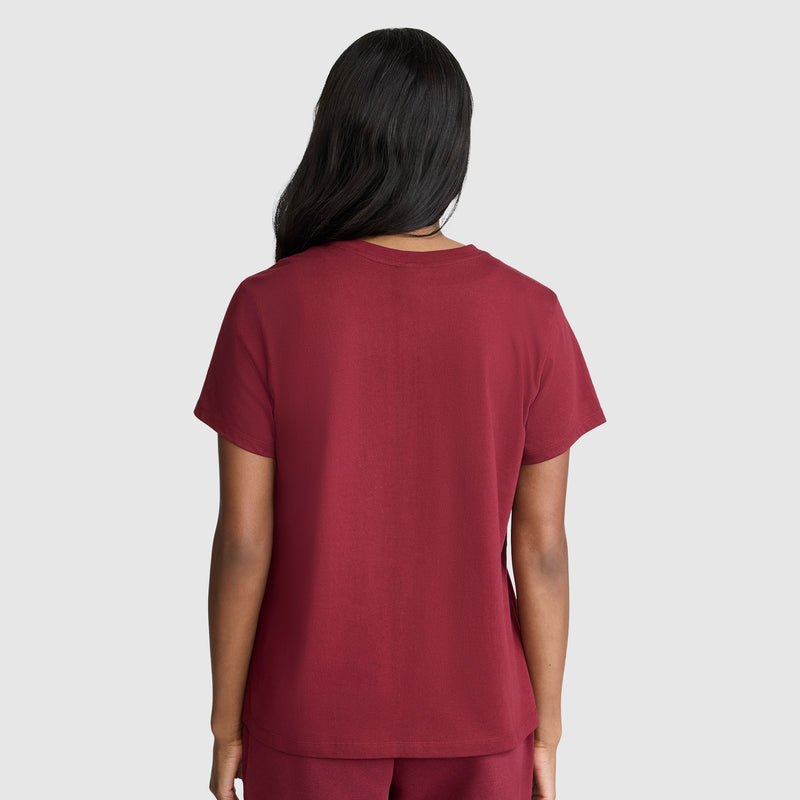 A person with long dark hair is seen from behind, wearing the Champion Classic T-Shirt with script logo in maroon and matching pants, standing against a plain light gray background.