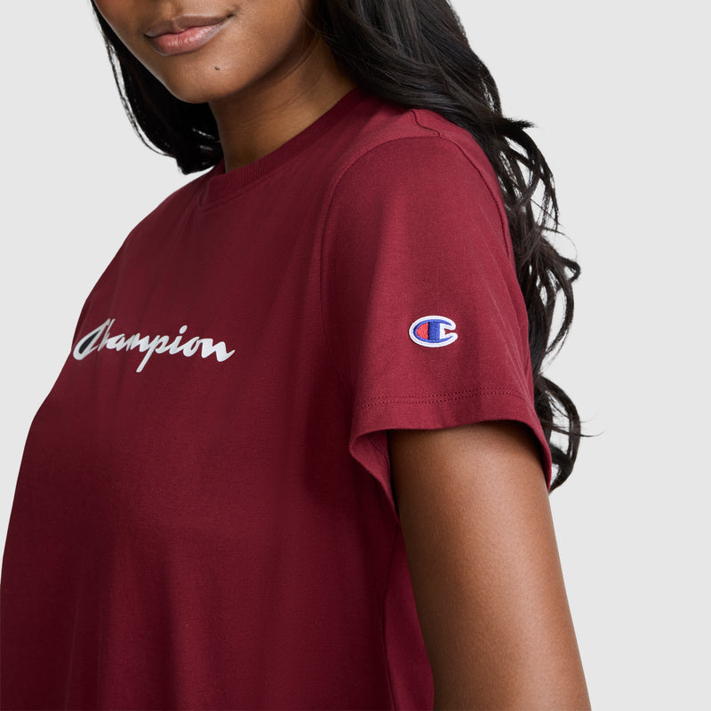 A woman wearing the Champion Classic T-Shirt, Script Logo—featuring the brand’s signature script logo across the chest and a small Champion patch on the sleeve—stands against a plain light background.
