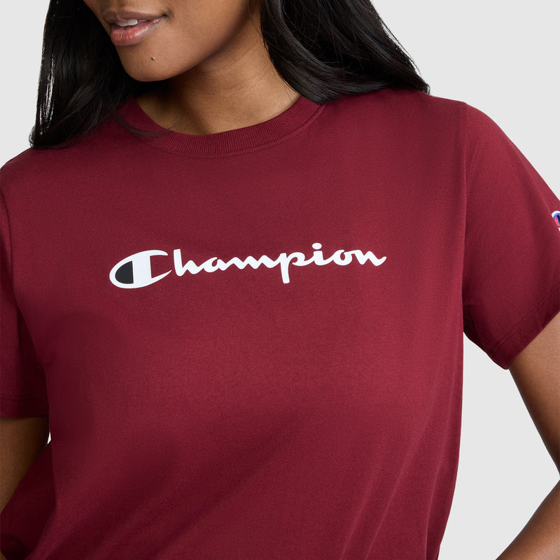A person shown from the shoulders to the waist, wearing a maroon Champion Classic T-Shirt, Script Logo, featuring the iconic white script logo across the chest against a plain background.