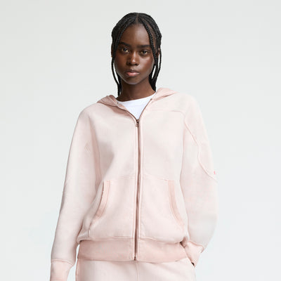 A person with braided hair wears a Champion Time Capsule Vintage 80's Full Zip Hoodie in light pink over a white shirt, standing against a plain white background with a neutral expression.