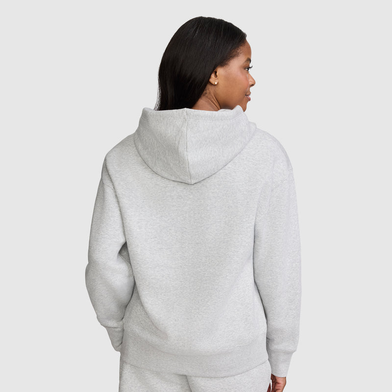A woman with long dark hair is shown from the back against a plain light gray background, wearing the Champion Tonal Script Freshman Powerblend Hoodie in light gray, paired with matching sweatpants.