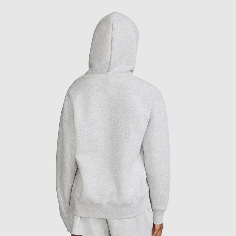 A person is seen from behind wearing a light gray Champion Tonal Script Freshman Powerblend Hoodie with matching shorts, displaying the back of the women’s hooded sweatshirt against a plain light background.