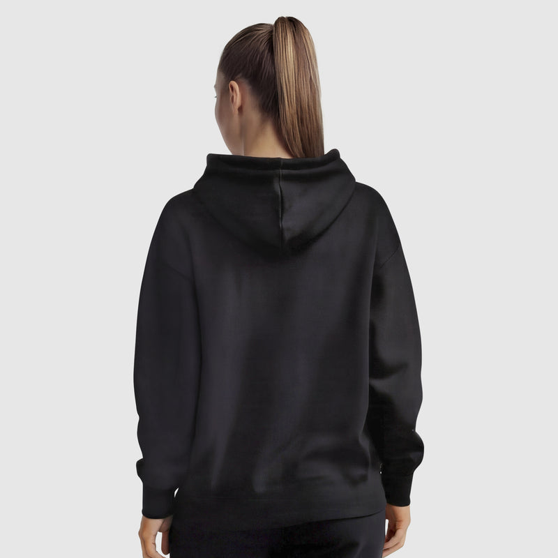 A woman with a high ponytail is seen from the back, wearing a black Champion Tonal Script Freshman Powerblend Hoodie and black pants, standing against a light gray background.