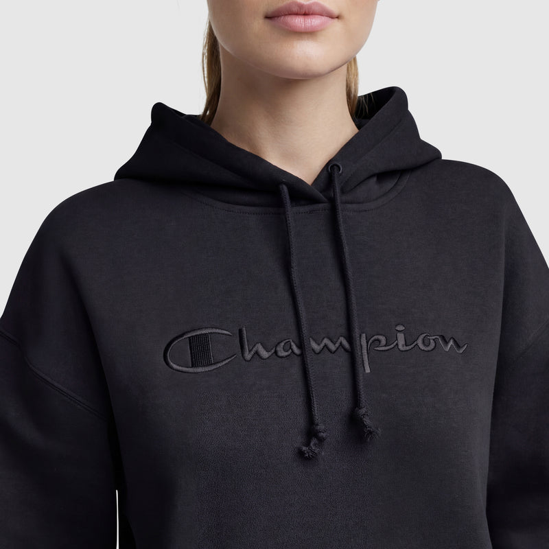 A person wears a Champion Tonal Script Freshman Powerblend Hoodie, featuring "Champion" embroidered in black on the front. Only the lower half of the face and upper torso of this women's pullover are visible.