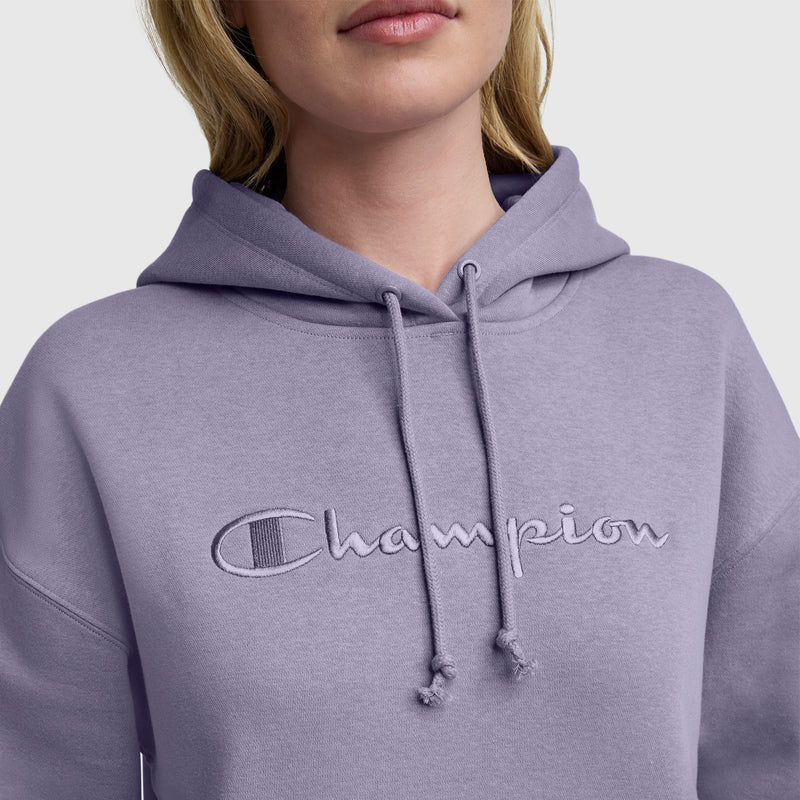 A person wears the Champion Tonal Script Freshman Powerblend Hoodie, a light purple women’s pullover featuring tonal "Champion" embroidery on the chest, shown from shoulders to upper face.