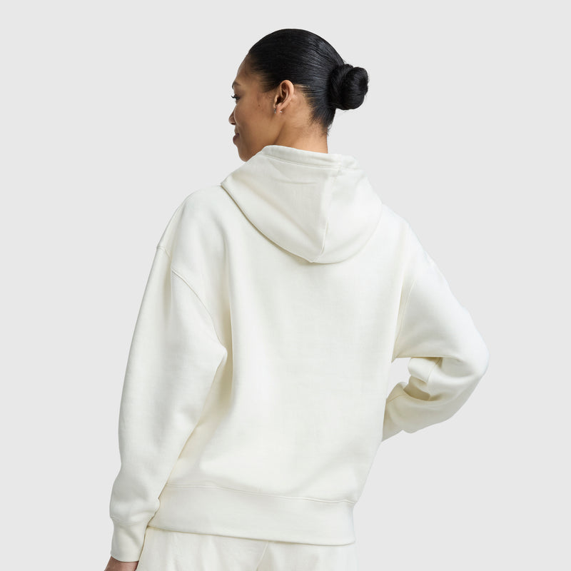 A person with dark hair in a bun is shown from the back, wearing an oversized Champion Tonal Script Freshman Powerblend Hoodie and matching pants against a plain light gray background.