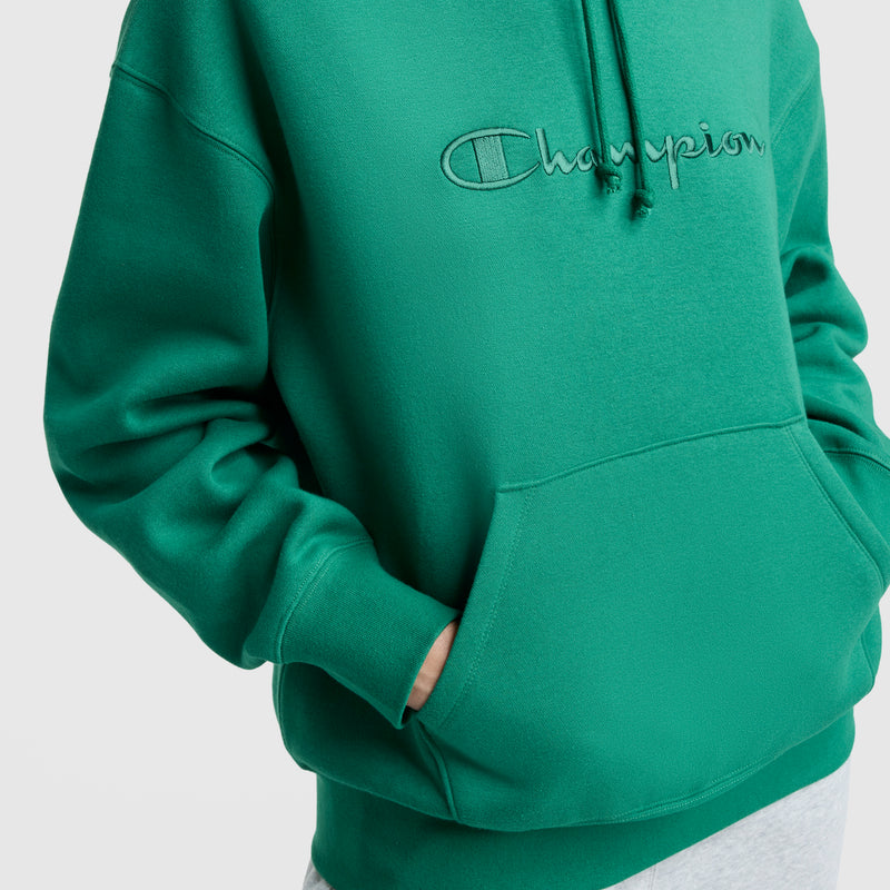 A person wears a cozy Champion Tonal Script Freshman Powerblend Hoodie in bright green, featuring a front pocket and embroidered script logo on the chest. Their hands are tucked in the pocket; only the torso of the sweatshirt is visible.