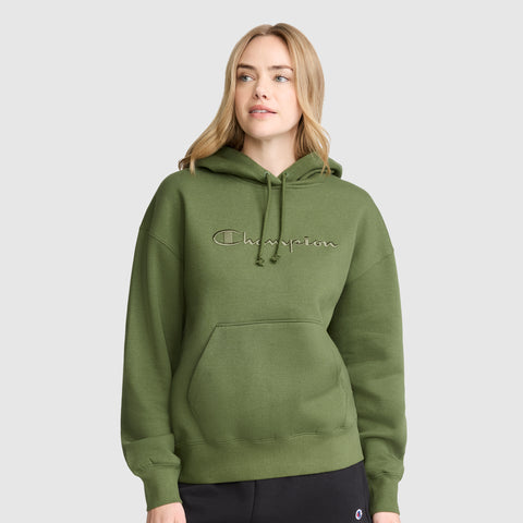 A woman wearing a Champion Tonal Script Freshman Powerblend Hoodie in olive green, featuring a front pocket, stands against a plain gray background, showcasing the comfortable style of this women’s hooded sweatshirt.