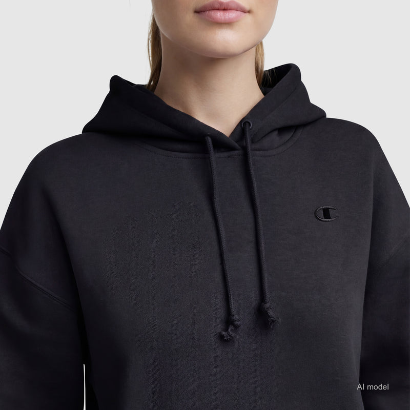 A person wears a black Champion Powerblend Freshman Hoodie, C Logo, shown from the shoulders up against a plain light background with the Champion logo visible on the left chest of this cozy women's sweatshirt.