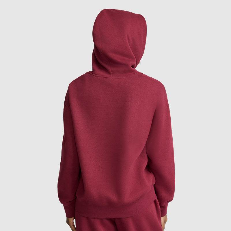 A person wearing a red Champion Small C Freshman Powerblend Hoodie and matching pants, seen from behind against a plain light gray background, showcases the comfort and style of this women’s hooded sweatshirt.