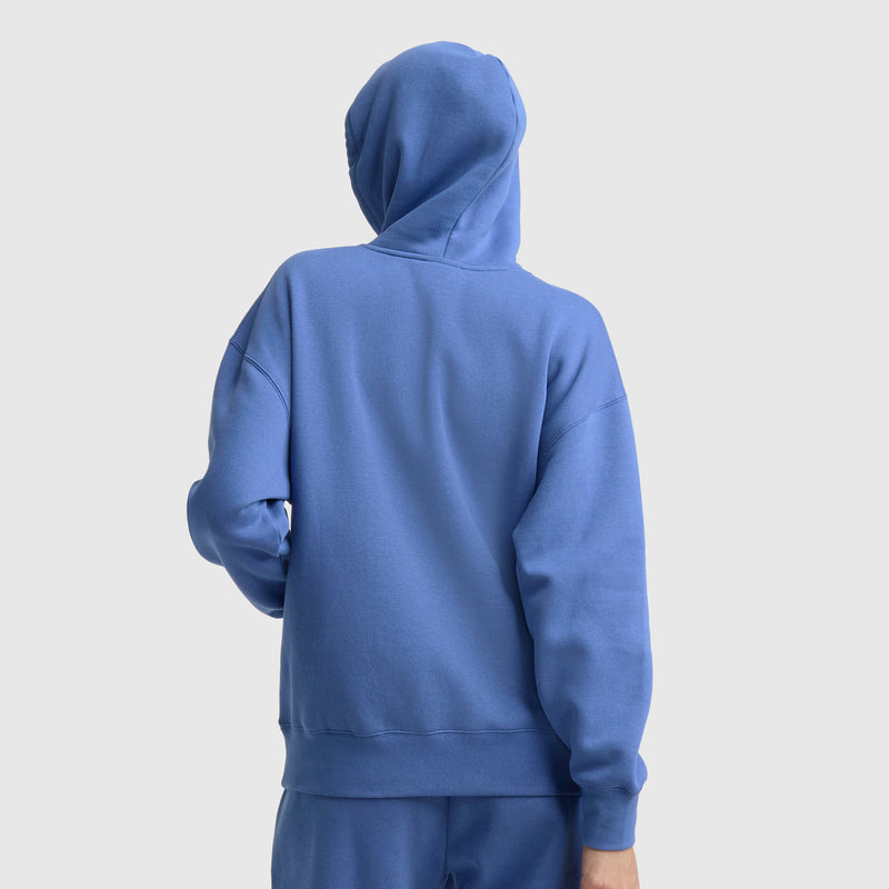A person wearing a blue Champion Small C Freshman Powerblend Hoodie and matching pants stands with their back to the camera against a plain light background.