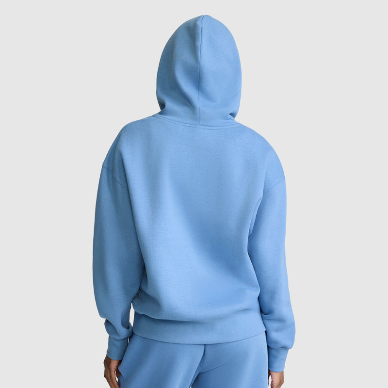 A person wearing a light blue Champion Small C Freshman Powerblend Hoodie and matching sweatpants stands facing away, hood up, against a plain light background, effortlessly showcasing authentic Champion style in this women’s hooded sweatshirt ensemble.