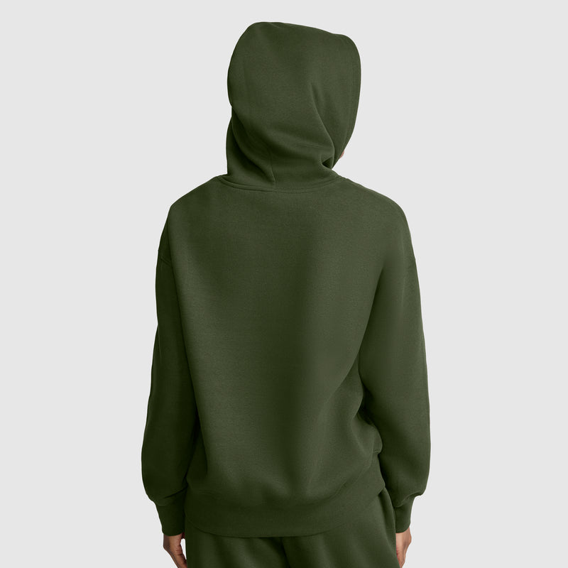 A person stands facing away with the hood up, wearing a dark green Champion Small C Freshman Powerblend Hoodie and matching pants, set against a plain light gray background.