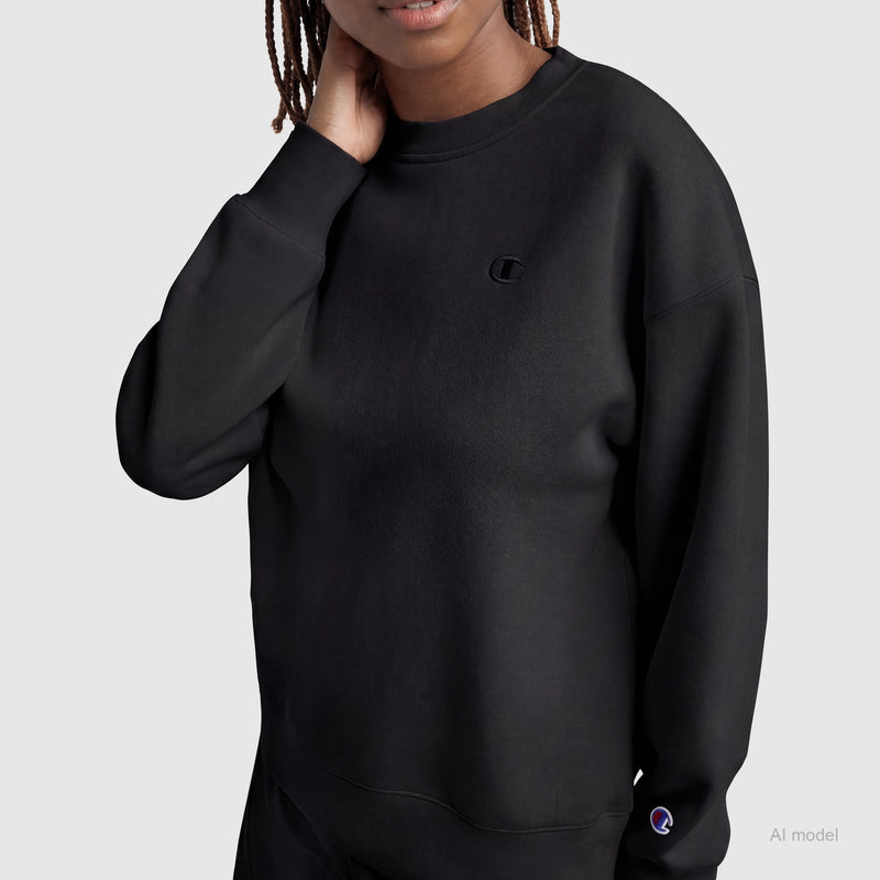 A person wears a Champion Powerblend Crewneck Sweatshirt, Small "C", in plain black against a light gray background, touching their neck. The sweatshirt features small Champion logos on the chest and sleeve.