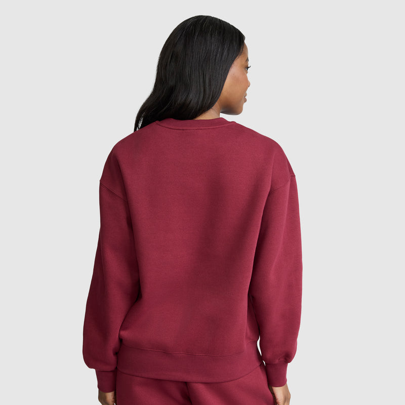 A person with long dark hair, seen from behind, is wearing a matching maroon Champion Powerblend Crewneck sweatshirt (featuring the Small “C” logo) and pants, standing against a plain light gray background.