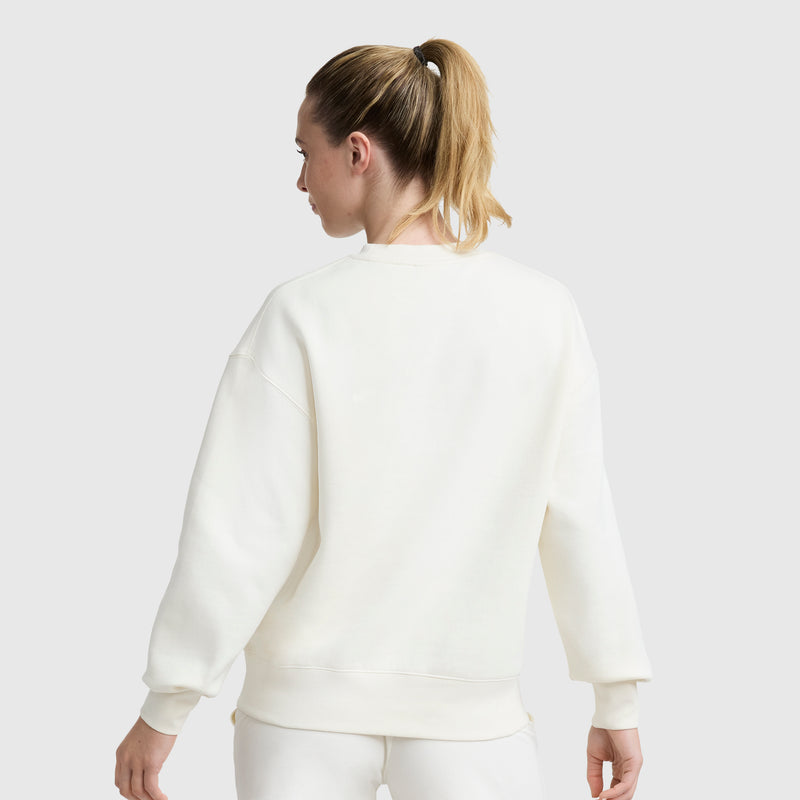 A woman with blonde hair in a ponytail is shown from the back, wearing a Champion Powerblend Crewneck, Small "C," and white pants against a plain light gray background.