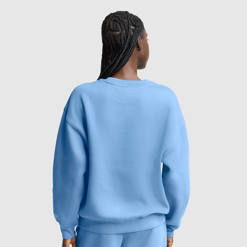 A person with braided hair, seen from behind, is wearing a loose, light blue Champion Powerblend Crewneck, Small “C” sweatshirt with matching pants against a plain light gray background.