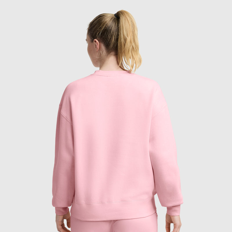 A woman with blonde hair in a ponytail wears a Champion Powerblend Crewneck Sweatshirt with embroidered script logo and matching pants, standing with her back to the camera against a plain light grey background.