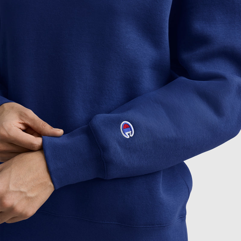 A person wearing the Champion Powerblend Crewneck Sweatshirt with an embroidered script logo, shown here in blue, adjusts their cuff to reveal the small red, white, and blue sleeve detail. Made from soft Powerblend fleece fabric, this women’s sweatshirt offers both comfort and warmth—perfect for everyday style.