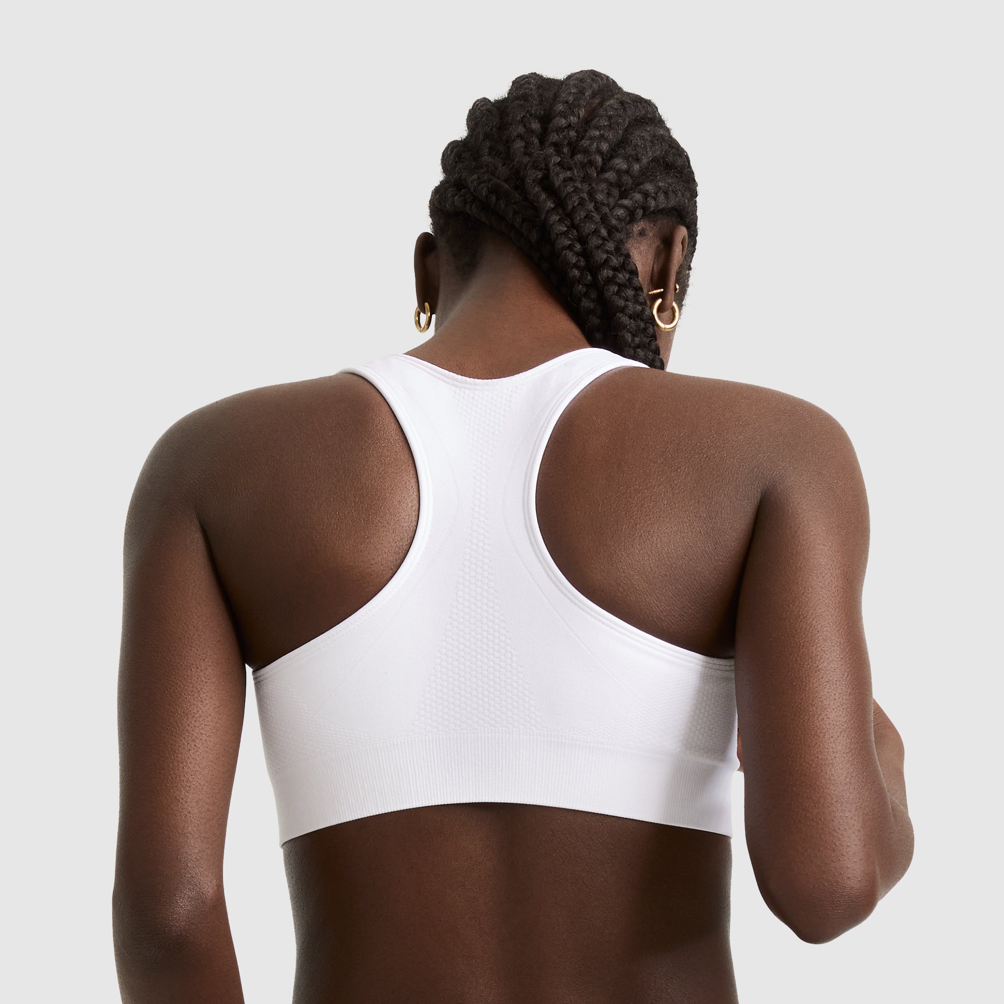 A woman with braided hair and gold hoop earrings models the Champion Seamless Racerback Sports Bra, shown from behind against a plain light gray background.
