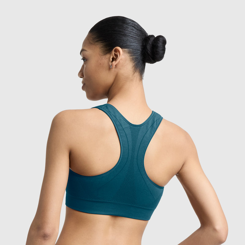 A woman with a sleek bun is shown from the back wearing the Champion Seamless Racerback Sports Bra in teal, set against a plain light gray background.
