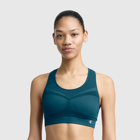 A woman models the Champion Seamless Racerback Sports Bra in teal, standing against a plain light gray background and looking at the camera with a neutral expression.