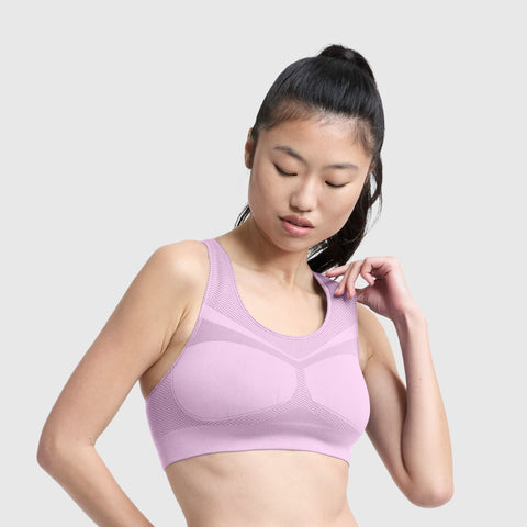 A woman with long dark hair in a high ponytail wears the Champion Seamless Racerback Sports Bra in light purple, featuring moisture-wicking fabric, as she looks down and touches the strap with her right hand. The background is plain light gray.