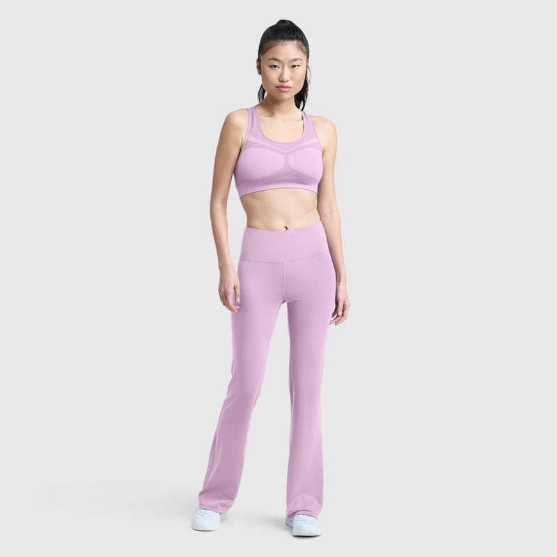 A person stands facing forward, wearing the Champion Seamless Racerback Sports Bra in light purple with moderate support and matching flared leggings, paired with white sneakers against a plain light gray background.