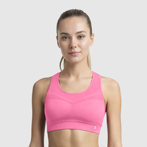 A woman with light skin and straight, light brown hair in a ponytail wears a bright pink Champion Seamless Racerback Sports Bra, standing against a plain light gray background and looking directly at the camera with a neutral expression.