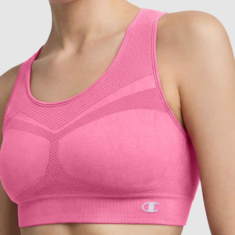 A person wears the Champion Seamless Racerback Sports Bra in bright pink, featuring textured panels and the Champion logo on the bottom left. The image shows only their upper torso and shoulders against a plain background.