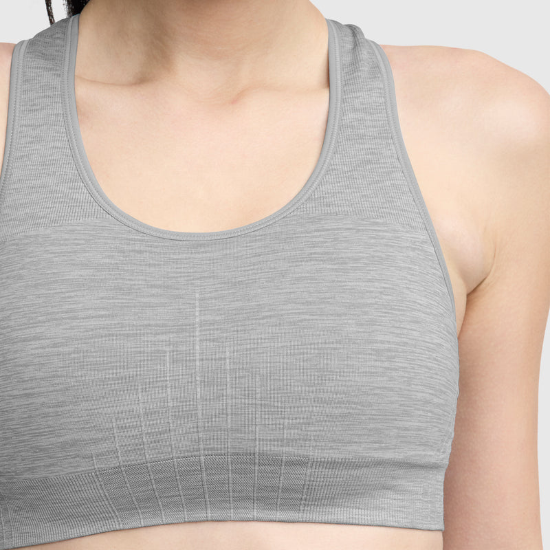 A person wears a Champion Infinity Racerback Sports Bra in light gray, shown from shoulders to upper waist against a plain background. This wireless sports bra features a seamless design with subtle vertical patterns.