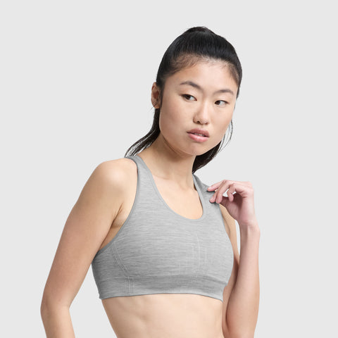 A woman with long dark hair in a high ponytail wears a light gray Champion Infinity Racerback Sports Bra, looking to her left against a plain light gray background.