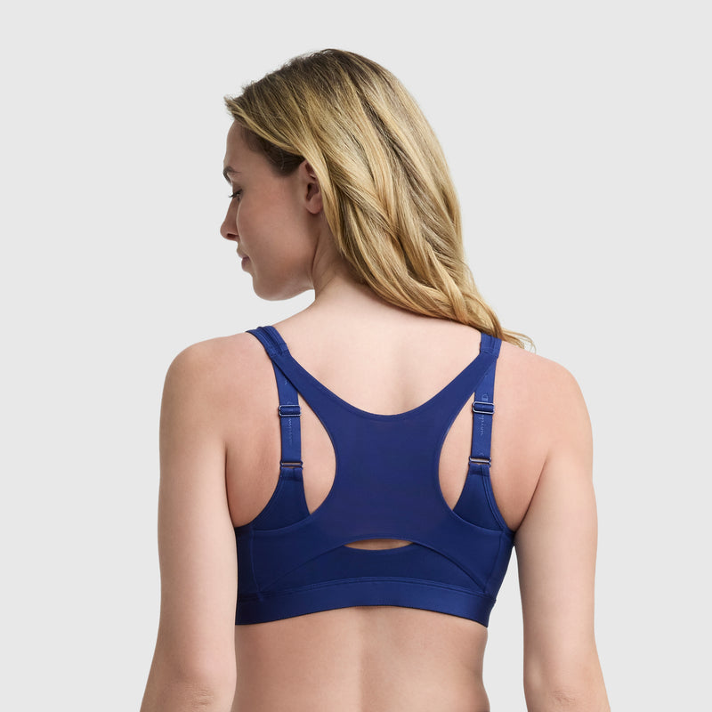 A woman with long blonde hair is seen from the back wearing the Champion Motion Control Zip Sports Bra in dark blue with adjustable straps, set against a plain light background.