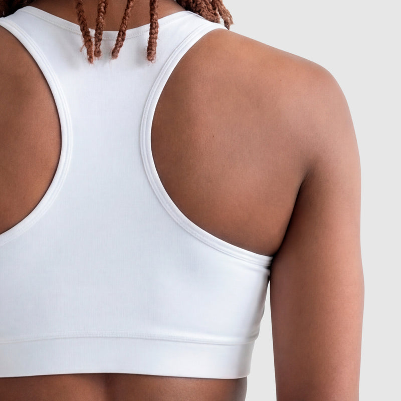 A close-up of a person with medium brown skin and long, thin, brown dreadlocks wearing the Champion Sports Bra, Script Logo in white cotton-spandex, set against a plain light gray background.