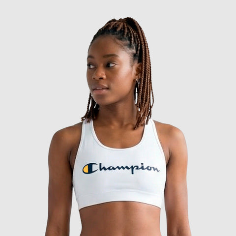 A woman with braided hair in a ponytail wears a Champion Sports Bra, Script Logo, made from soft cotton-spandex. She looks to the side against a plain, light gray background.