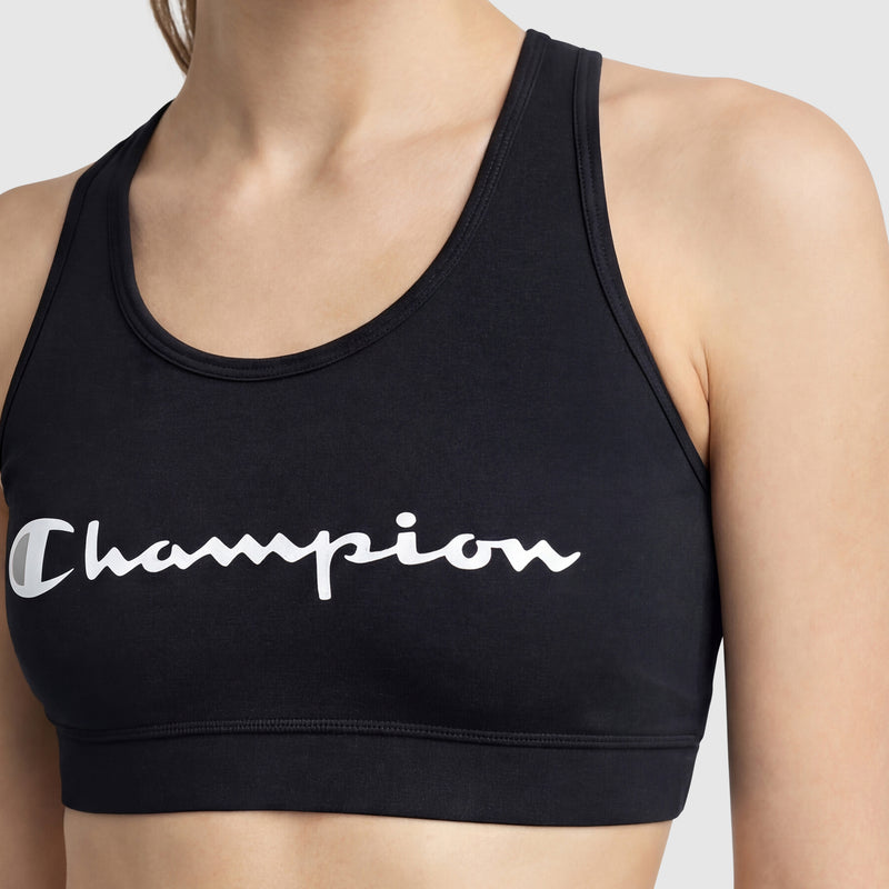 A person wears the Champion Sports Bra, Script Logo, a black cotton-spandex jersey. "Champion" is scripted in white across the chest. Only the upper torso is visible in the image.