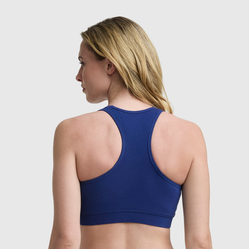 A woman with blonde hair is shown from the back, wearing a blue Champion Sports Bra with a script logo against a plain light background.