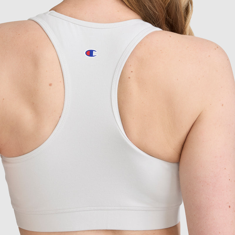 A person is shown from the back, wearing the Champion Sports Bra, Script Logo in white. This racerback cotton-spandex bra features a small Champion logo on the upper back and provides an athletic fit, with the image captured against a neutral background.