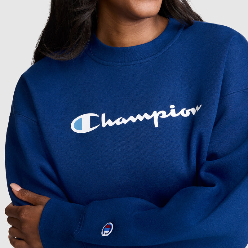 A person wearing the Champion Powerblend Crewneck Sweatshirt, Script Logo—a royal blue women’s crewneck featuring the signature white Champion script across the chest and a small logo patch on the sleeve. Made from cozy Powerblend fleece, this sweatshirt offers a blend of comfort and timeless style.
